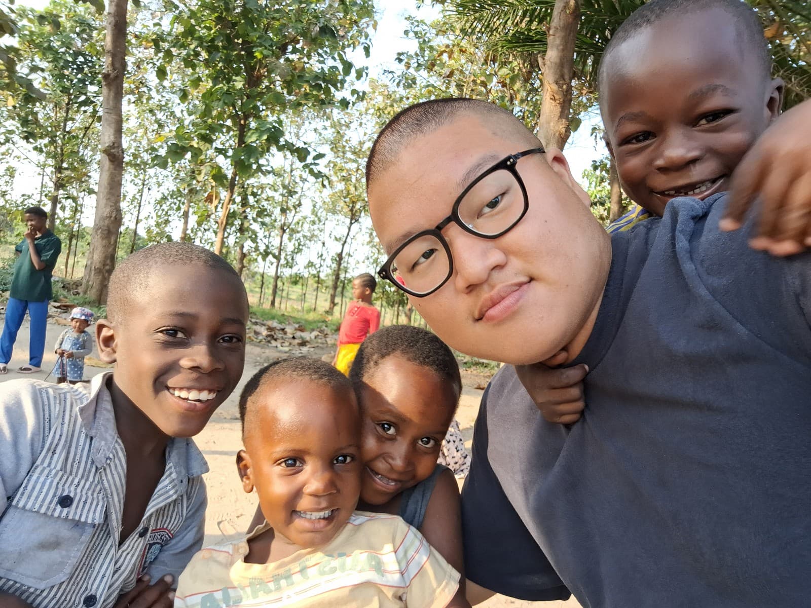An Asian volunteer taking a selfie with smiling children in a rural outdoor setting
